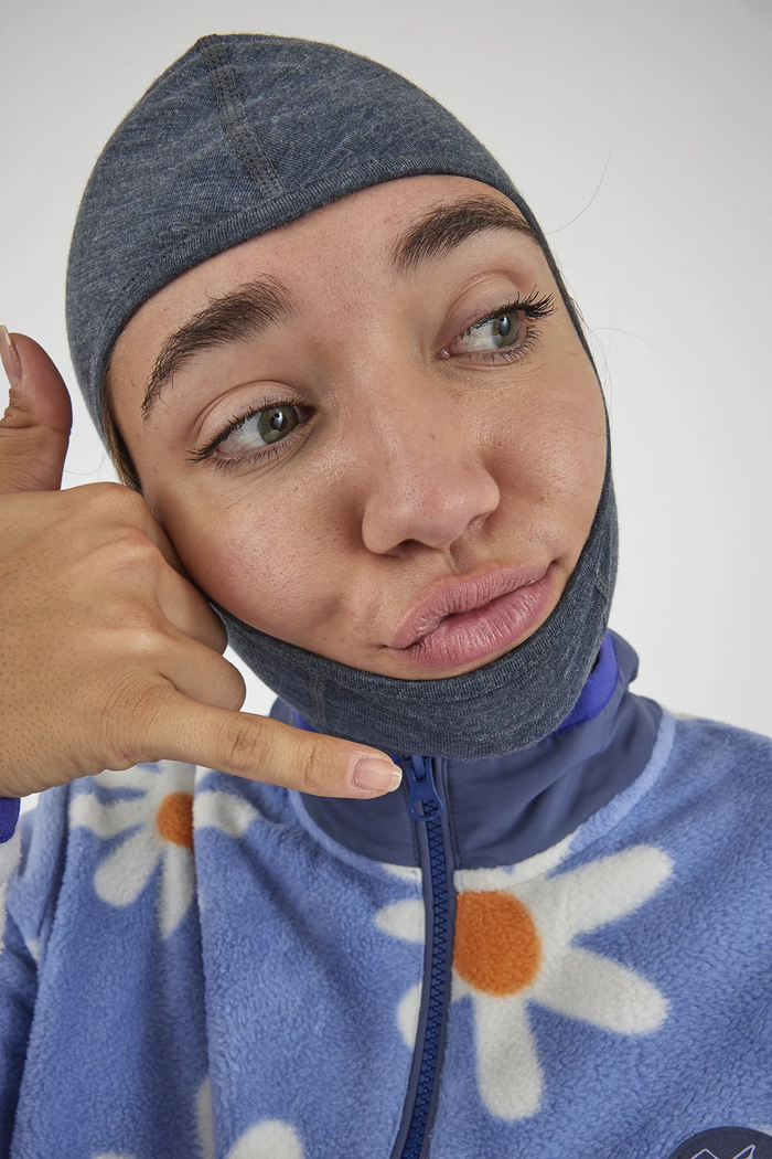 Person wearing a blue hoodie with floral patterns and a gray head covering, making a hand gesture.