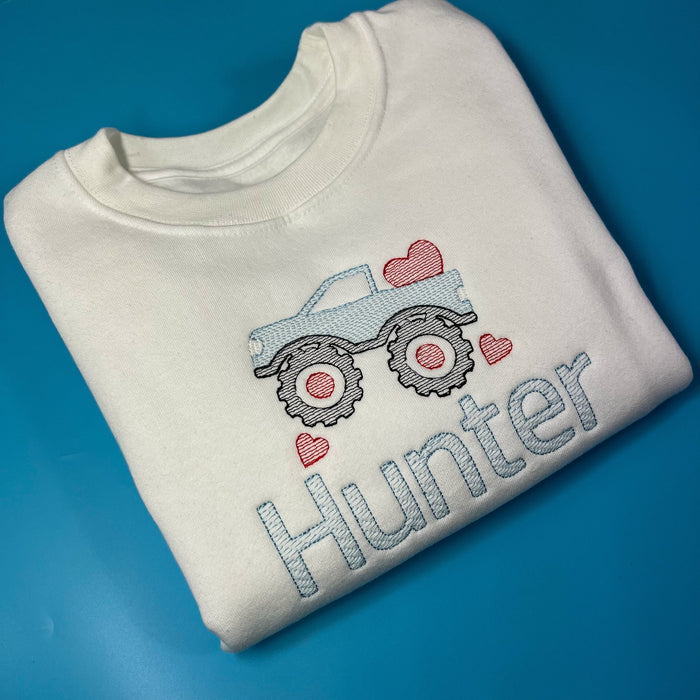 White sweatshirt with a monster truck on the front with love hearts in embroidery