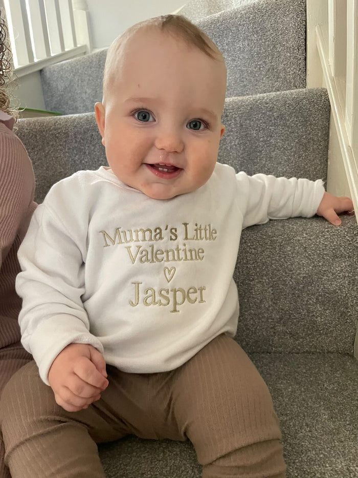 Baby wearing a white sweatshirt with 'Mumma's Little Valentine Jasper' text, sitting on a staircase.