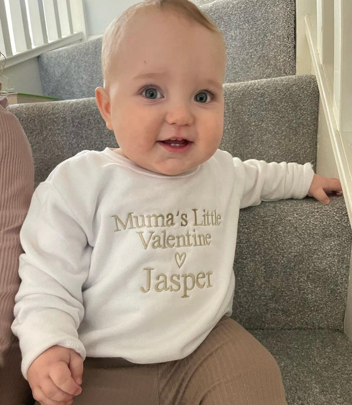 Baby wearing a white sweatshirt with 'Mumma's Little Valentine Jasper' text, sitting on a staircase.