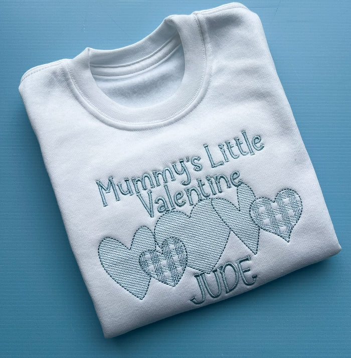 Folded white sweatshirt with embroidered text and hearts on a blue background