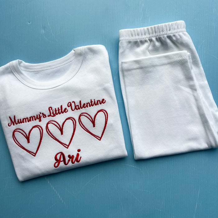 White pyjamas with 'Mummy's Little Valentine Ari' text and hearts on a blue background