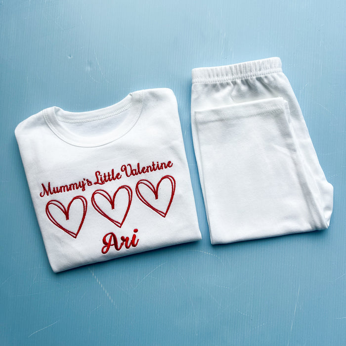 White t-shirt with red text and hearts and white pants on a blue background