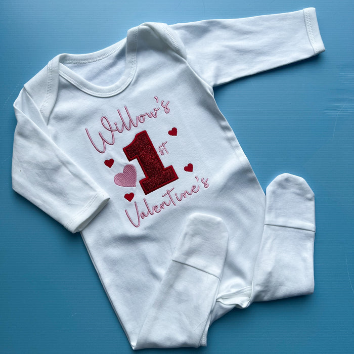 White baby onesie with 'Willow's 1st Valentine's' text on a blue background