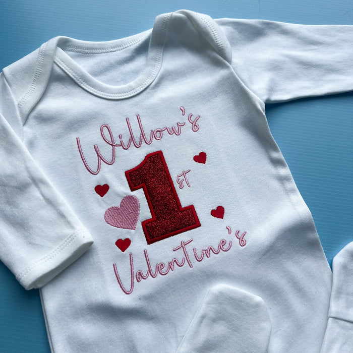White baby onesie with red and pink text and heart designs on a blue background