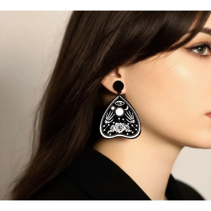 Occult Rose Planchette Earrings in black acrylic with white skeleton hands, rose, eye, moon, and star graphics model wearing