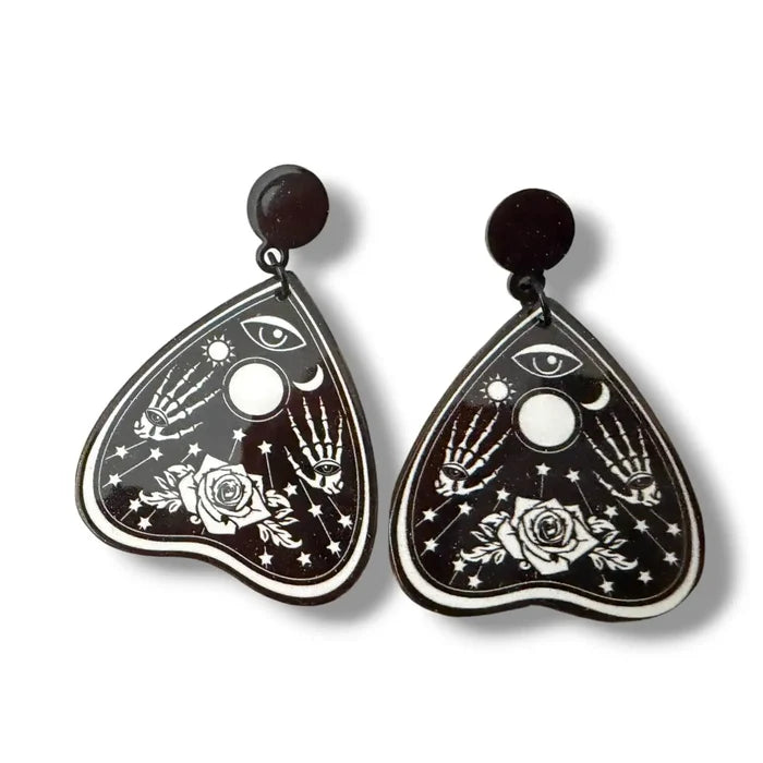 Occult Rose Planchette Earrings in black acrylic with white skeleton hands, rose, eye, moon, and star graphics flat lay