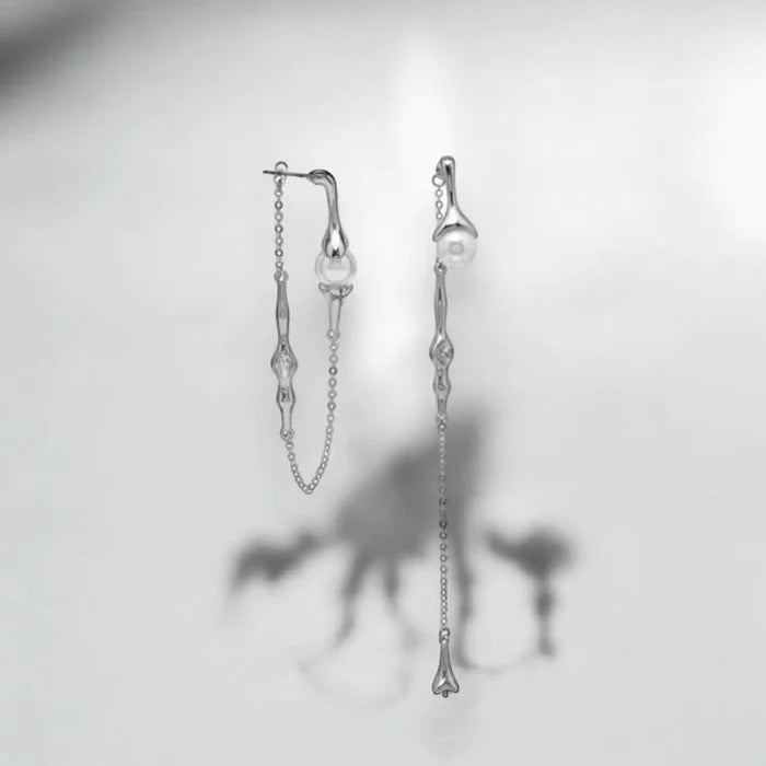 Silver asymmetrical pearl drop earrings with silver curb chains, simulated white pearls, and crystal accents, modern gothic and Y2K fashion jewelry.
