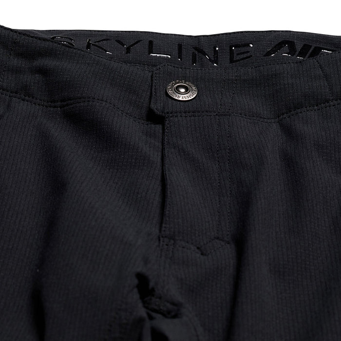 Close-up of black pants with a button and 'SKYLINE' branding.