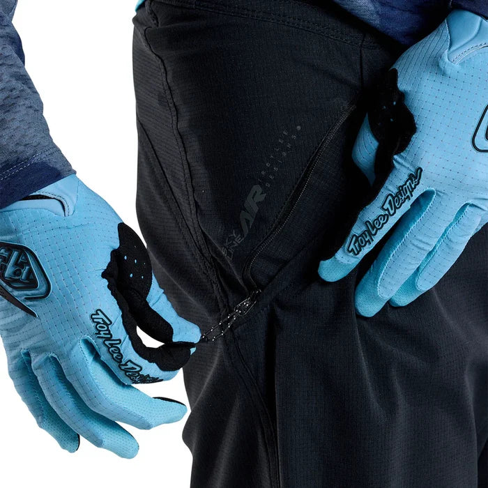 Person wearing black pants and blue gloves with 'Troy Lee Designs' branding on a white background