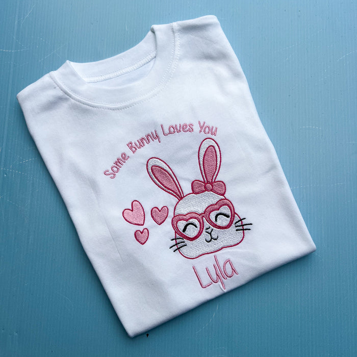 Folded white t-shirt with embroidered bunny design and text on a blue background