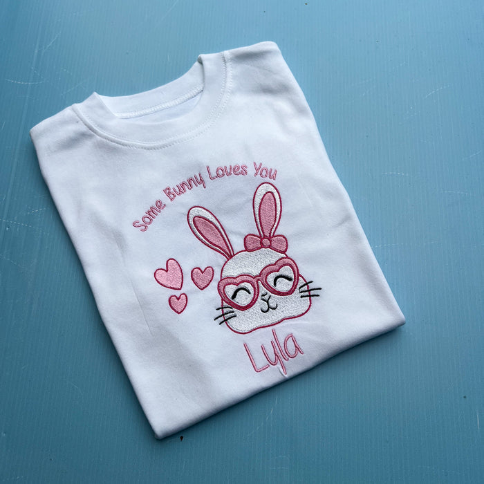 White t-shirt with embroidered bunny design and text on a blue surface