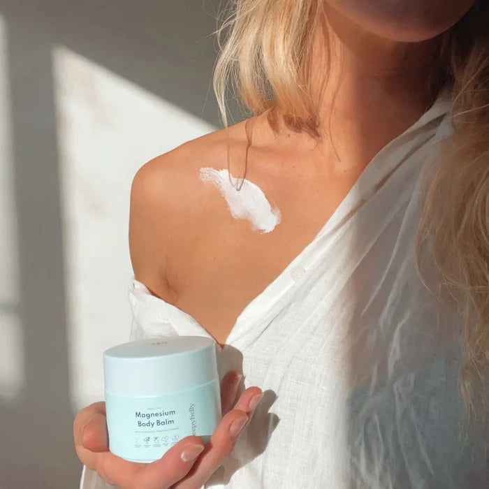 Woman applying Sleepybelly Magnesium Body Balm to her shoulder while holding the light blue tub