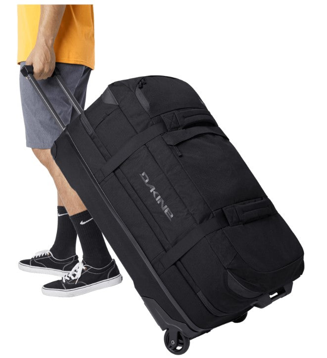 Person pulling a black Dakine suitcase on wheels