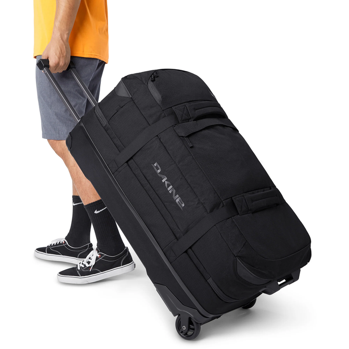Person holding a black DAKINE suitcase on wheels with a white background