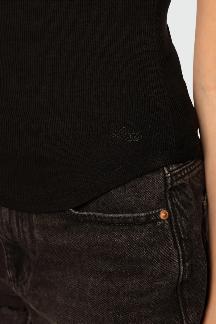 Person wearing a black sleeveless top and dark jeans with a visible brand logo.