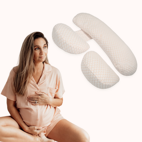 Pregnant woman in peach pyjamas beside the blush three-piece pregnancy pillow from the Sweet Dreams Bundle