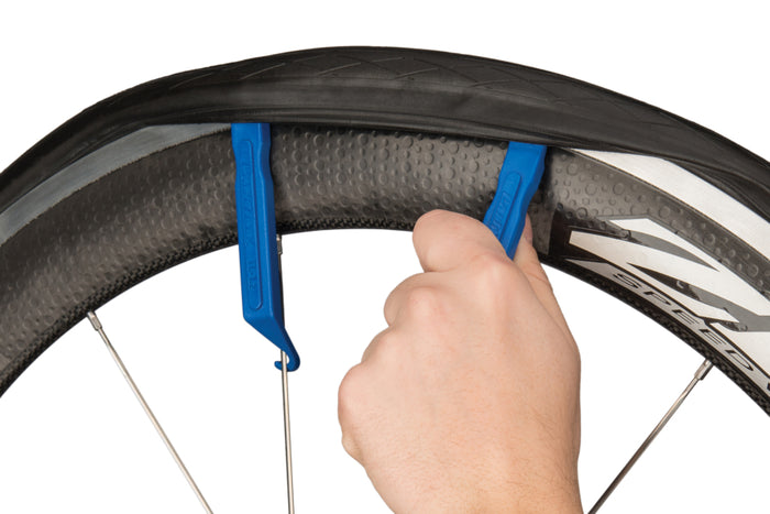 Hand using a blue tire lever to remove a bike tire.