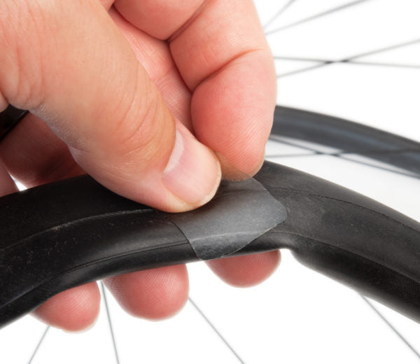 Hand applying a patch to a bicycle tire with a white background