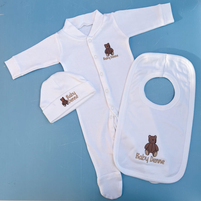 Baby clothing set with white onesie, hat, and bib on a blue background