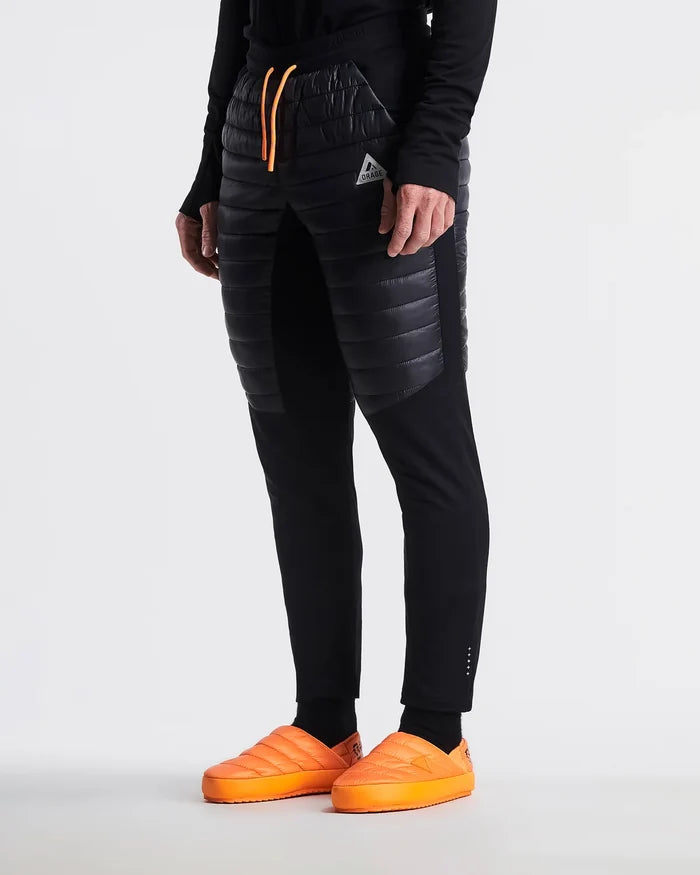 Person wearing black puffer pants with orange accents and orange shoes on a white background