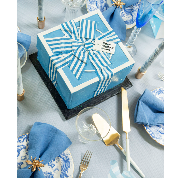 Gold bee-shaped napkin ring holding a blue linen napkin on a white and blue floral plate.