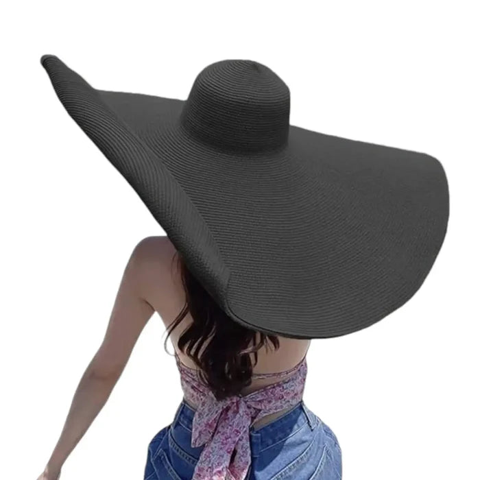woman wearing the black Women’s Oversized Brim Straw Sun Hat with dramatic 10-inch asymmetrical brim and woven straw beach style