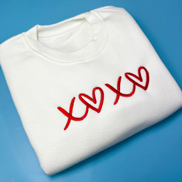 Folded white sweatshirt with red embroidery saying XOXO